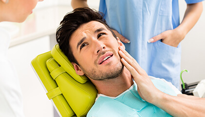 Male patient grimacing holding cheek in dental chair