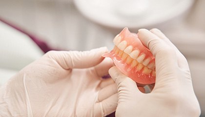 Gloved hands holding full set of dentures
