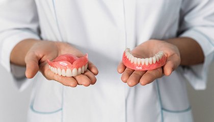 Someone holding a complete arch of dentures in each hand in front of their abdomen