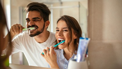 Man and woman together at bathroom mirror brushing teeth