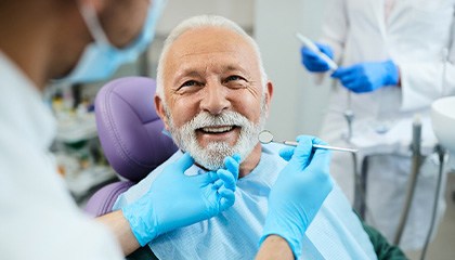 Dentist in blue gloves holding chin of man about to examine his teeth