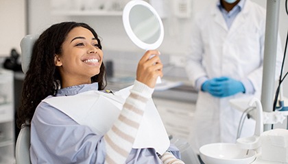 Woman smiling at reflection in handheld mirror