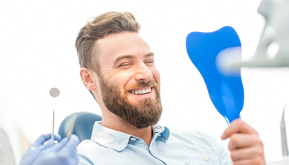 Man in dental chair looking at smile in mirror