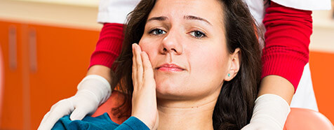 Frowning woman in dental chair holding cheek