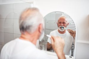 mature man brushing his teeth in bathroom