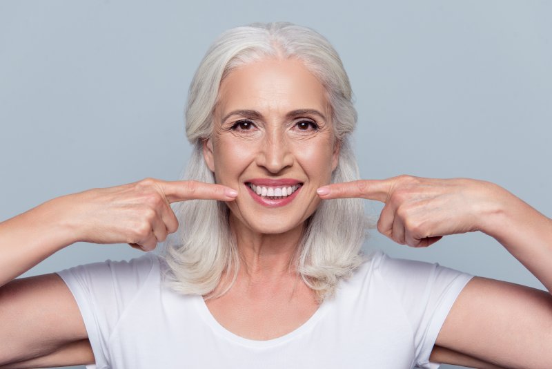 Elderly woman smiling and pointing at her teeth