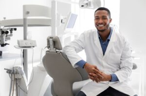 Dentist smiling and sitting on dentist&rsquo;s chair.